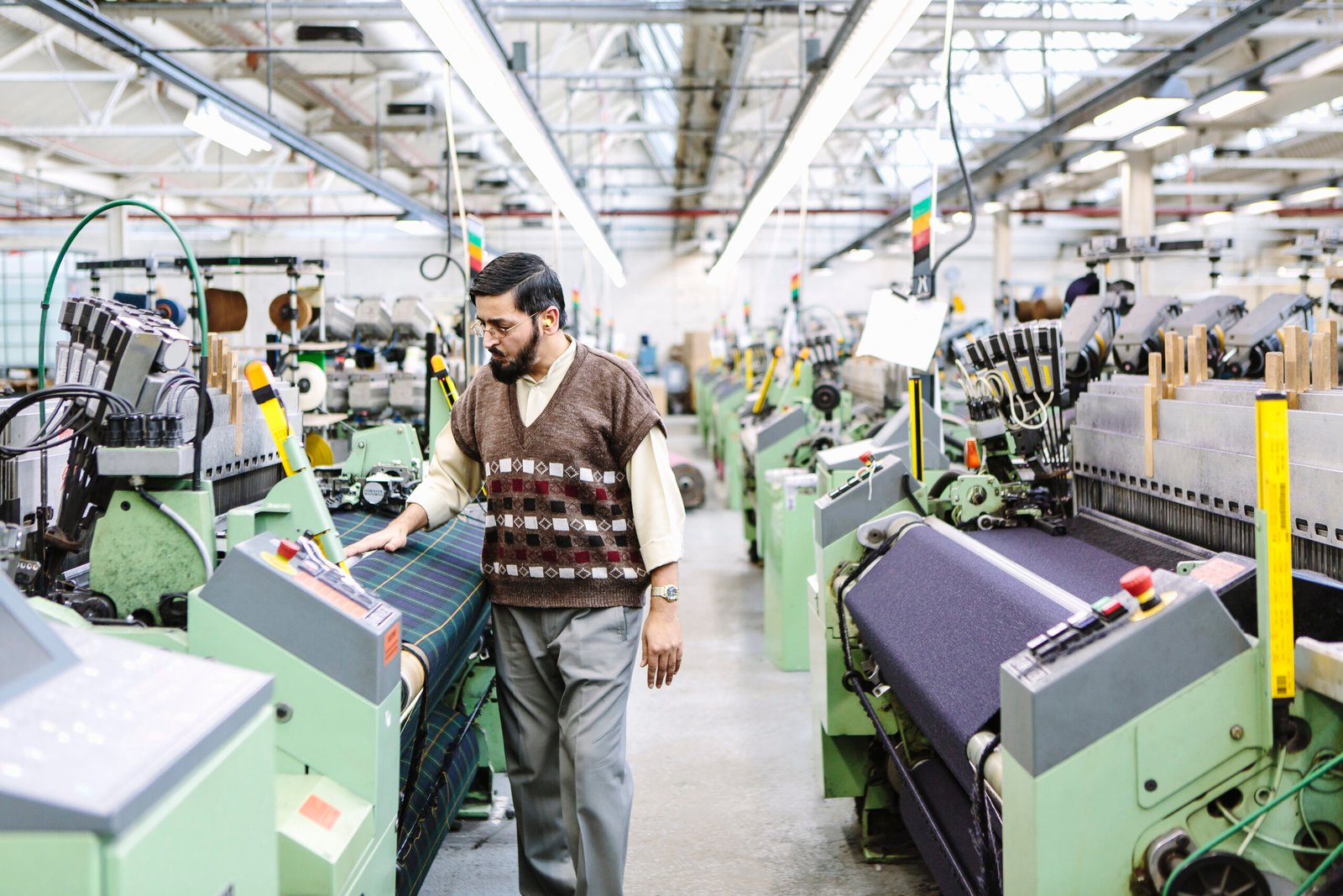 Male factory worker monitoring weaving machine quality in woollen mill