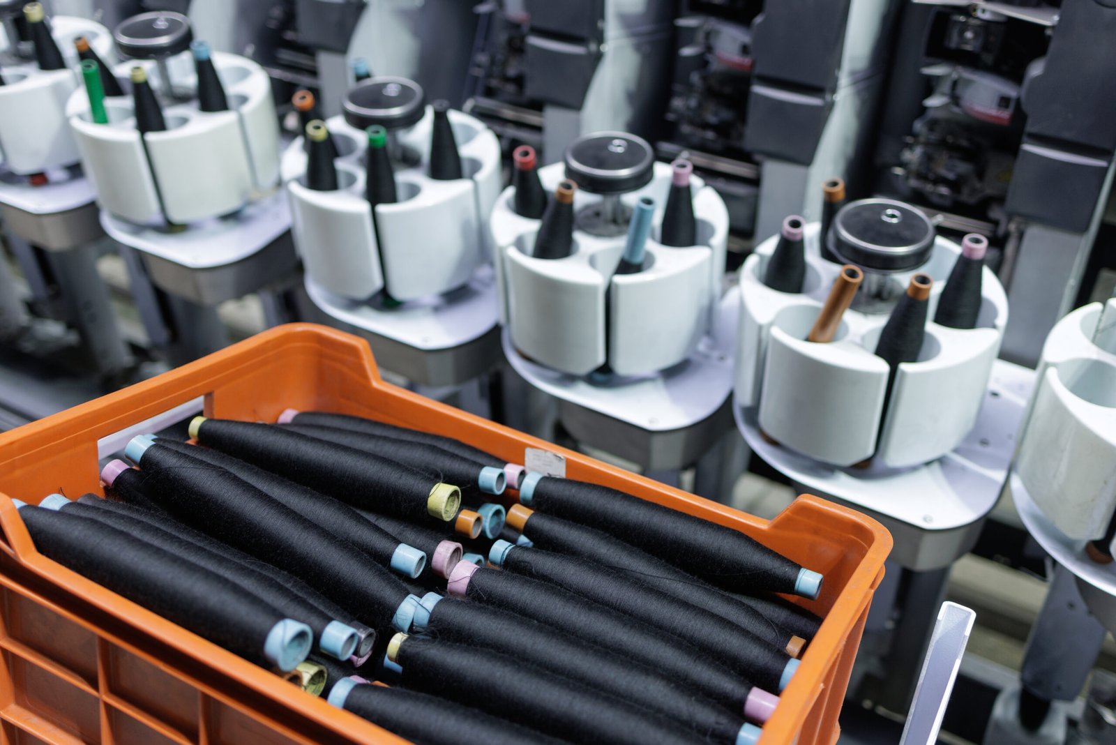 A close-up view of a wool spinning factory showcasing spools of thread in an orange container beside advanced spinning machines, highlighting the weaving process.